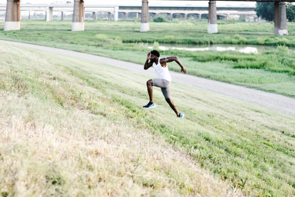 a picture of a man running up a grassy hill daylight background