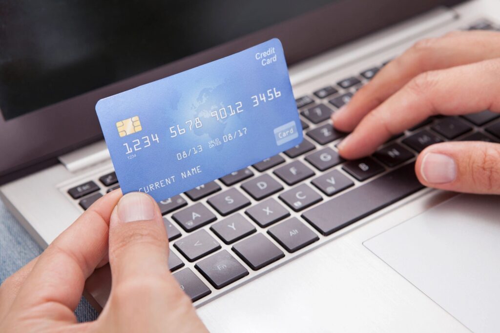 a picture of someone holding their credit card with one hand and typing on the keyboard with the other