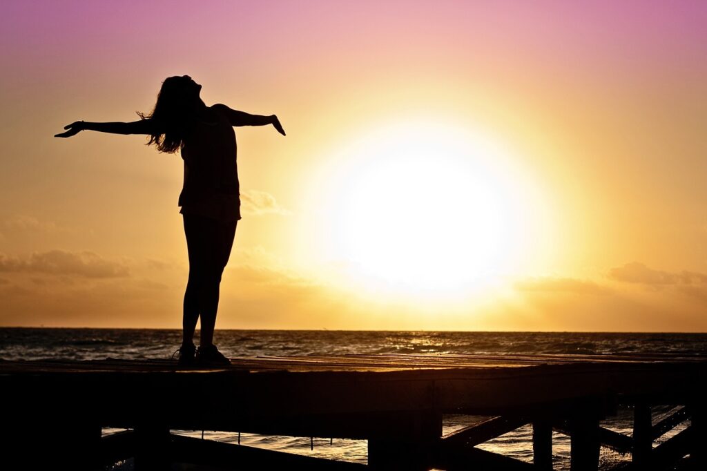 woman with her arms extended horizontally towards the sunset over a beach