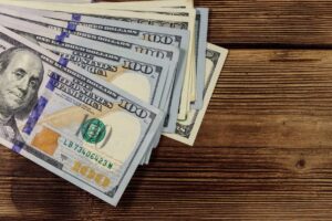 A picture of $100 bills slightly spread out on a wooden table