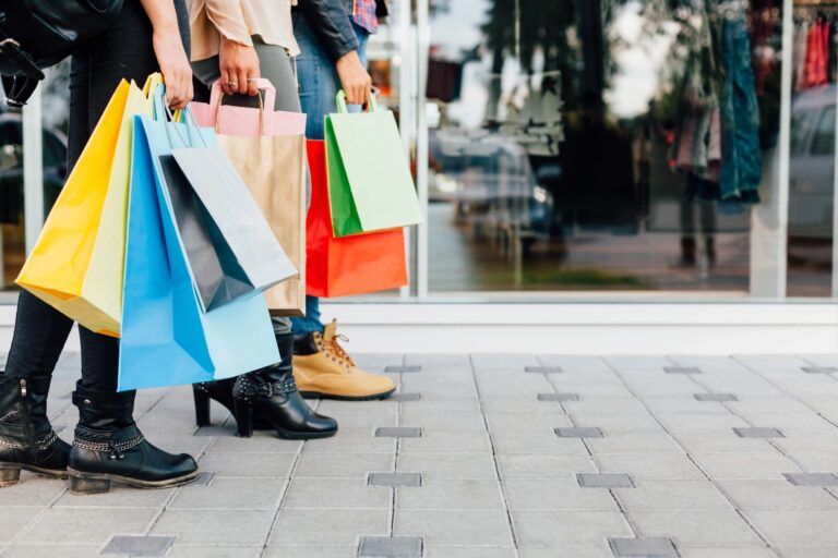 A picture of a line of people holding different colored bags that you would get at a mall after shopping